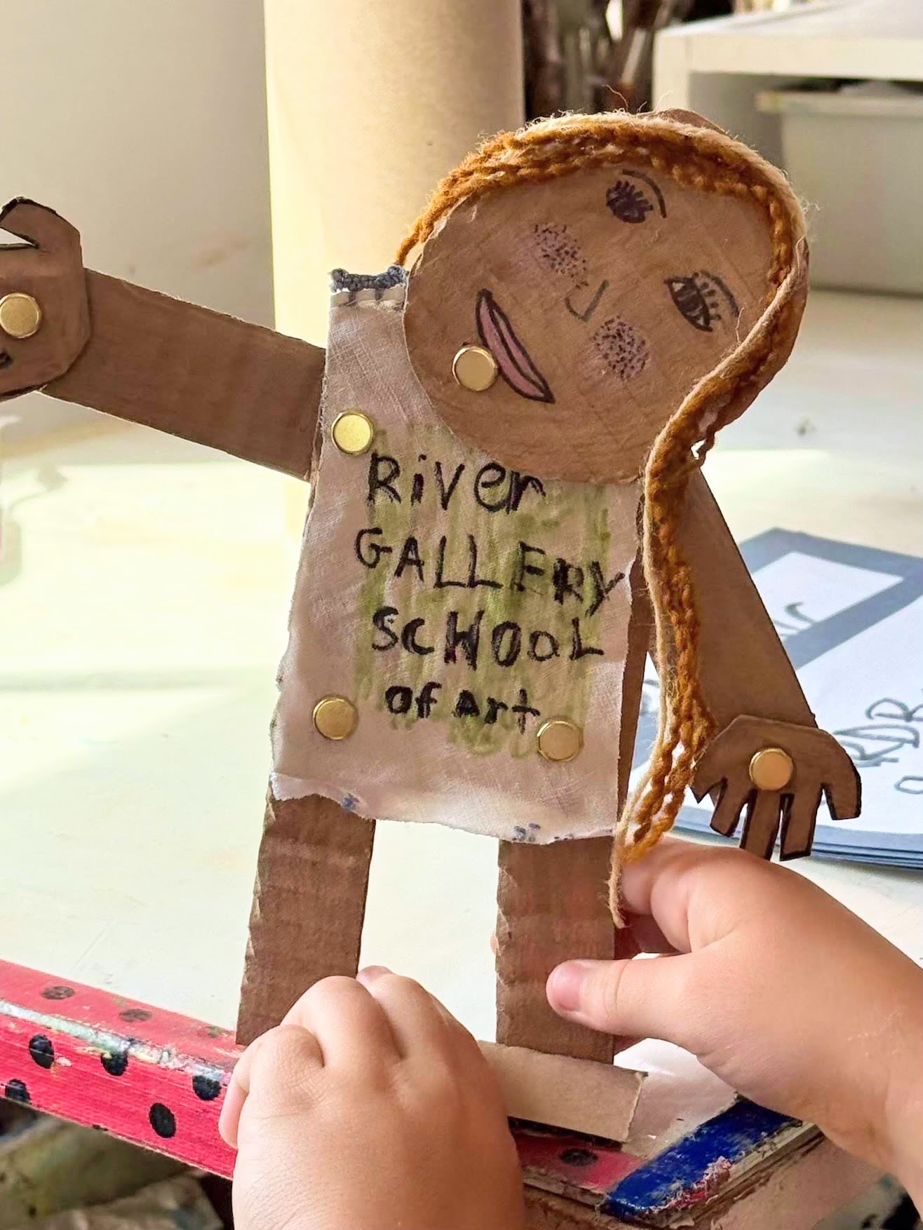 Cardboard cutout figure of a whimsical girl with "River Gallery School of Art" written on her shirt.