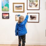 Child in blue jacket pointing to a favorite painting at River Gallery School's annual Off the Wall preview exhibition